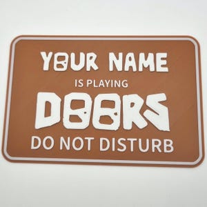 May include: A brown sign with white text that reads "YOUR NAME IS PLAYING DOORS DO NOT DISTURB".
