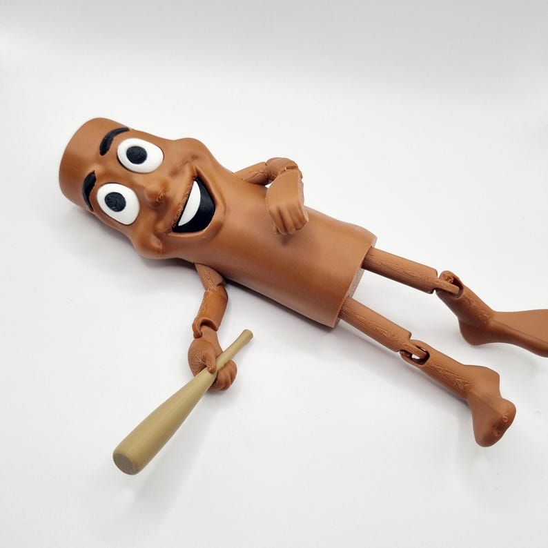 Puede incluir: Una figura de juguete articulada de color marr&oacute;n que representa a un personaje de dibujos animados sonriente que sostiene un bate de b&eacute;isbol de madera. La figura tiene un cuerpo marr&oacute;n con una cara humana y ojos grandes. La figura est&aacute; tumbada de espaldas con las piernas extendidas.