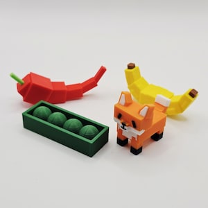 K&ouml;nnte beinhalten: Eine Sammlung geometrischer Figuren, 3D-gedruckt. Enth&auml;lt eine rote Chilischote, eine gr&uuml;ne Schachtel mit Erbsen, eine gelbe Banane und einen orangefarbenen Fuchs. Die Figuren sind im Pixel-Design gestaltet.