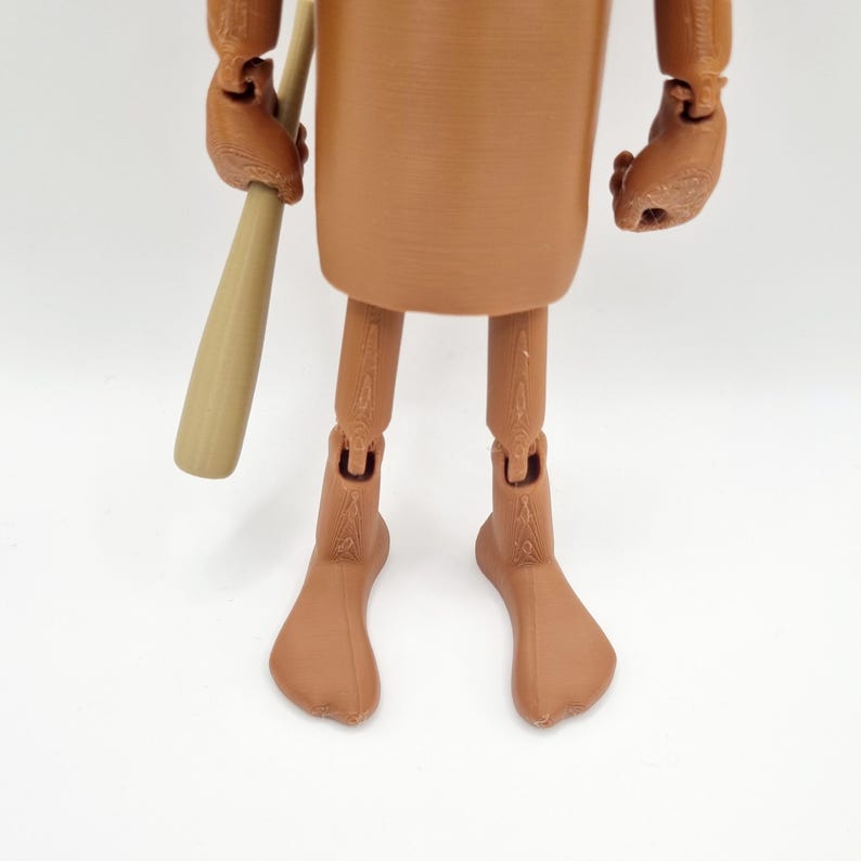 Puede incluir: Una figura de acci&oacute;n articulada marr&oacute;n con un bate de b&eacute;isbol de madera. La figura tiene un dise&ntilde;o simple y lleva una t&uacute;nica marr&oacute;n.