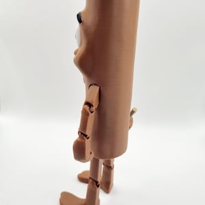 Puede incluir: Una figura articulada marr&oacute;n con un cuerpo largo y cil&iacute;ndrico y una cabeza grande y redonda. La figura tiene un solo ojo grande y una nariz peque&ntilde;a y puntiaguda. Los brazos y las piernas de la figura est&aacute;n articulados en las articulaciones, lo que permite una variedad de poses.