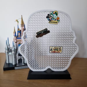 May include: A white, patterned display stand shaped like a character's head, with Disney pins attached. A miniature Disney castle is to the left. The pins read "SOARIN", "I'D RATHER BE AT DISNEYLAND", and "Walt Disney World".