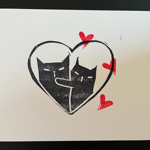May include: Two black cats are inside a heart shape with red hearts around it. The cats are facing each other and appear to be hugging.