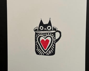 May include: A black cat peeking out of a white mug with a red heart design.