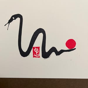 Peut inclure: Dessin &agrave; l'encre noire et blanche d'un serpent avec un cercle rouge et un tampon rouge avec le caract&egrave;re chinois "生" sur fond blanc.