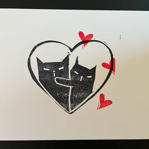 May include: Two black cats are drawn inside a heart shape with red hearts around the outside. The cats are facing each other and appear to be hugging.