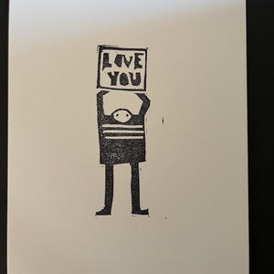 May include: A black and white illustration of a person holding a sign that says "LOVE YOU".