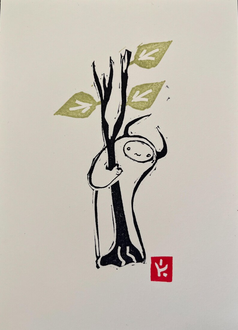 May include: A black and white illustration of a small, white creature hugging a tree with green leaves. The creature has a simple, smiling face. A red stamp with a black symbol is in the bottom right corner.
