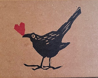 Op de afbeelding: Een zwarte vogel met een rood hart op zijn snavel, gedrukt op een bruine achtergrond.