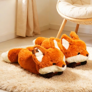 May include: A pair of plush fox slippers. The slippers are orange with white accents on the ears and tail. They have a brown nose and a soft, furry texture. The slippers are lying on a beige rug.