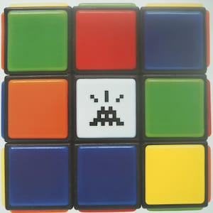 Peut inclure: Un cube puzzle coloré avec un design extraterrestre pixélisé rétro sur un carré. Les autres carrés sont de différentes couleurs : vert, rouge, bleu, orange et jaune. Un jouet classique.