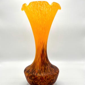 May include: A tall glass vase with a flared, ruffled rim. The color transitions from a bright, translucent orange at the top to a deep, mottled brown and red base. The glass features a vertical, streaked pattern throughout the body.