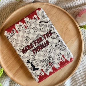 May include: A rectangular e-reader cover featuring a gray and white checkered pattern with a crime-themed design. It displays red glittery blood drips, a magnifying glass, a fingerprint, and the text "HERE FOR THE THRILLS" in bold red letters.