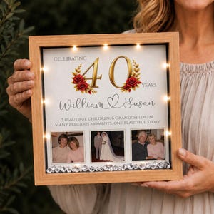 May include: A square light wood shadow box frame with internal LED lights, featuring a 40th anniversary design with red roses, the names William and Susan, and three photos. The text reads Celebrating 40 Years, 5 beautiful children, 6 grandchildren.