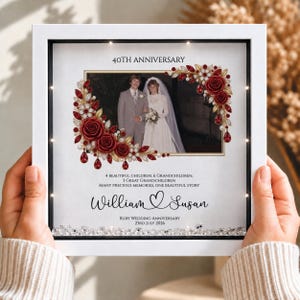 May include: A white square shadow box frame containing a wedding photograph, decorated with red and gold floral embellishments and clear crystals. The text reads 40TH ANNIVERSARY, William and Susan, and Ruby Wedding Anniversary 23rd July 2026.