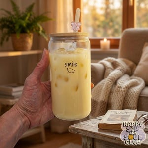Könnte beinhalten: Ein klares Glas mit Bambusdeckel und einem hellen Getränk mit Eiswürfeln. Auf dem Glas steht das Wort smile in schwarzen Kleinbuchstaben mit einer kleinen geschwungenen Linie darunter. Ein durchsichtiger Strohhalm mit einem rosa Schmetterling ist eingesteckt.