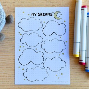 May include: A white printable sheet with the title "My Dreams" and a crescent moon. The sheet has nine cloud shapes for writing in, surrounded by small gold stars.