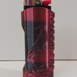 May include: A red, black, and silver lighter with a black bird design and a floral pattern at the bottom. The lighter has a textured finish and says "S.H.I.E.L.D." on the side.