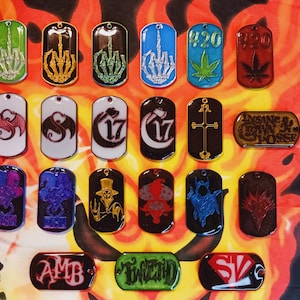 May include: Collection of metal dog tags with various designs. Includes tags with a skeleton hand giving the middle finger, marijuana leaf, and other graphics. The tags are in various colors and shapes.