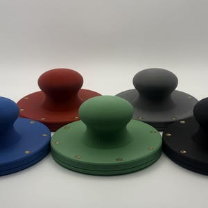 May include: Five circular, flat-bottomed tools with central handles, arranged in a cluster. Each tool features a distinct matte color: blue, red, green, gray, and black. Small, evenly spaced metallic rivets are embedded around the perimeter of each base.