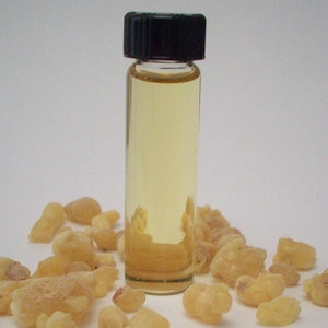 May include: A small glass bottle with a black cap filled with a light yellow liquid. The bottle is surrounded by small, irregularly shaped, light brown pieces of resin.