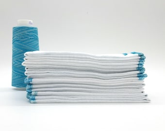 May include: A stack of white fabric squares with teal stitching and a spool of teal thread. The thread is wound in a crisscross pattern. The fabric squares are neatly folded and stacked.