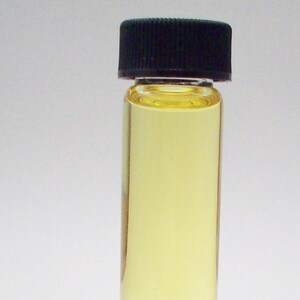 May include: A small glass bottle with a black lid filled with a light yellow liquid. The bottle is sitting on a clear surface.