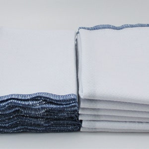 May include: A stack of white kitchen towels with blue trim. The towels are folded and stacked neatly.
