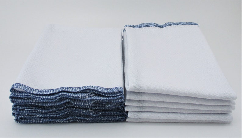 May include: A stack of white kitchen towels with blue trim. The towels are folded and stacked neatly.