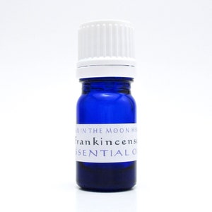 A cobalt blue glass bottle of Frankincense essential oil. The shape of the bottle is squat and the cap is ribbed and white. It is labeled Man in the Moon Herbs Frankincense Essential Oil.