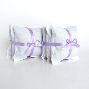 2 bundles of lavender dryer sachets. The sachets are square white muslin. There are 3 sachets in each bundle which is formed with a narrow lavender colored satiny ribbon wrapped around the sachets and tied in a bow like a gift box.