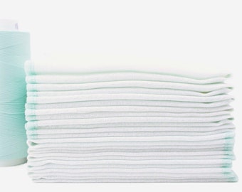 May include: A stack of white cotton cloths folded neatly, with a light blue edge. The cloths are arranged in a pile, with the top cloth folded in half.