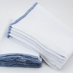 May include: A stack of white kitchen cloths with blue edging. The cloths are folded and stacked neatly.