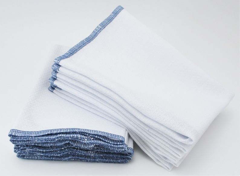 May include: A stack of white kitchen cloths with blue edging. The cloths are folded and stacked neatly.