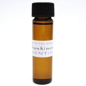 May include: A small amber glass bottle with a black lid. The bottle has a white label with purple text that reads "In the Moon Frankincense Essential".