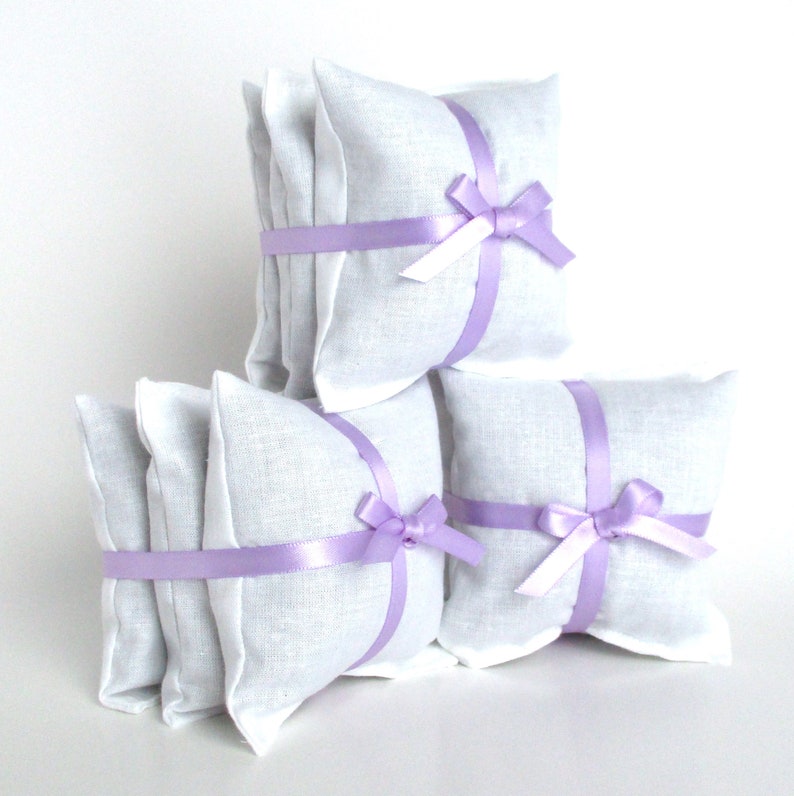 3 bundles of lavender dryer sachets. The sachets are square white muslin. There are 3 sachets in each bundle which is formed with a narrow lavender colored satiny ribbon wrapped around the sachets and tied in a bow like a gift box.