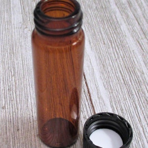 May include: A small amber glass bottle with a black screw-on lid. The bottle is empty and the lid is off.