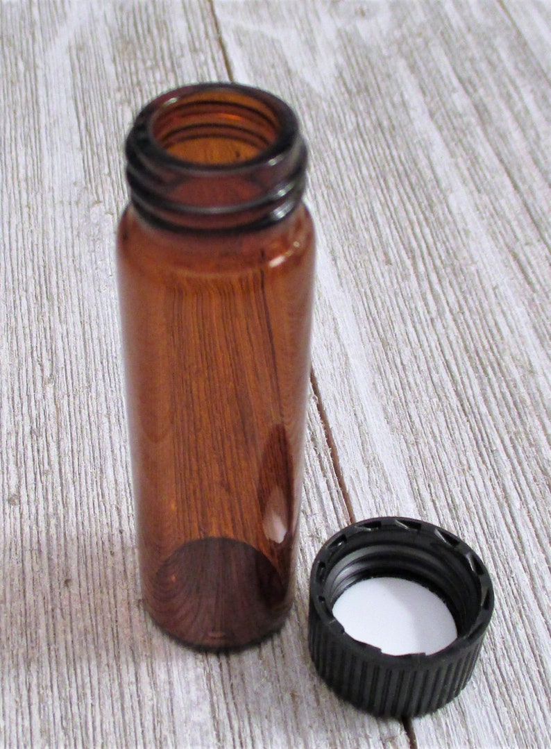 May include: A small amber glass bottle with a black screw-on lid. The bottle is empty and the lid is off.