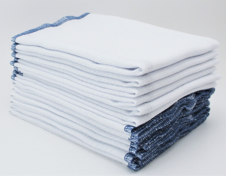 May include: A stack of white cotton dishcloths with blue edging. The cloths are folded and stacked neatly.