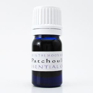 A cobalt blue glass bottle of patchouli essential oil. The shape of the bottle is squat and the cap is ribbed and white. It is labeled Man in the Moon Herbs Patchouli Essential Oil.