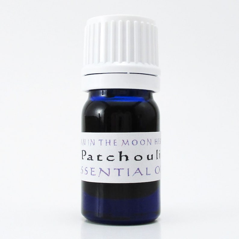 A cobalt blue glass bottle of patchouli essential oil. The shape of the bottle is squat and the cap is ribbed and white. It is labeled Man in the Moon Herbs Patchouli Essential Oil.