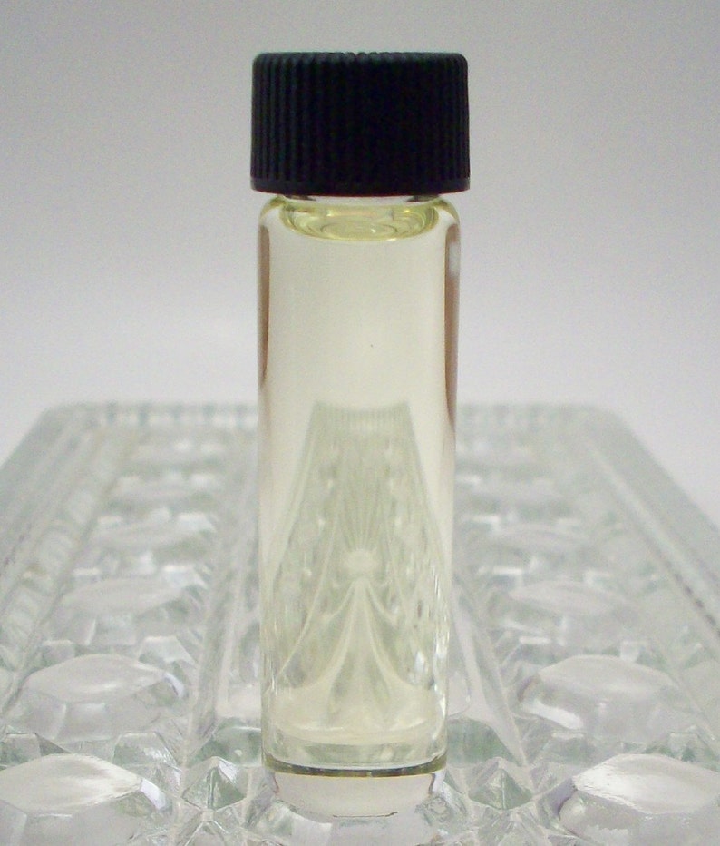 May include: A small clear glass bottle with a black screw-on cap, filled with a light yellow liquid. The bottle is sitting on a clear glass surface.