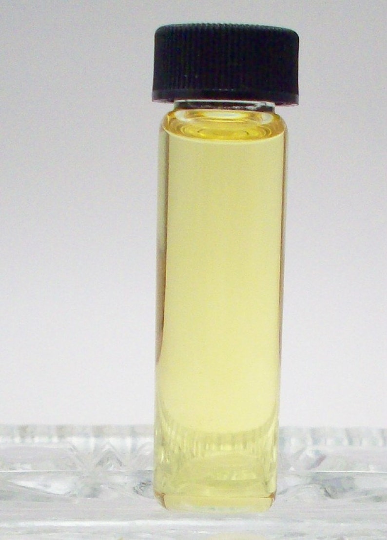 May include: A small glass bottle with a black lid filled with a light yellow liquid. The bottle is sitting on a clear surface.