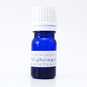 May include: A small blue glass bottle with a white cap. The bottle has a white label that reads "Nightingale Essential Oil".