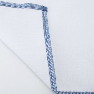 May include: A white fabric square with a blue stitched border.
