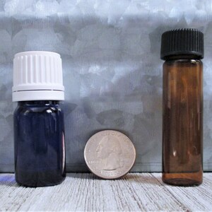 May include: Two glass bottles with different colored caps. The bottle on the left has a white cap and a dark blue body. The bottle on the right has a black cap and a brown body. A US quarter is shown for scale.
