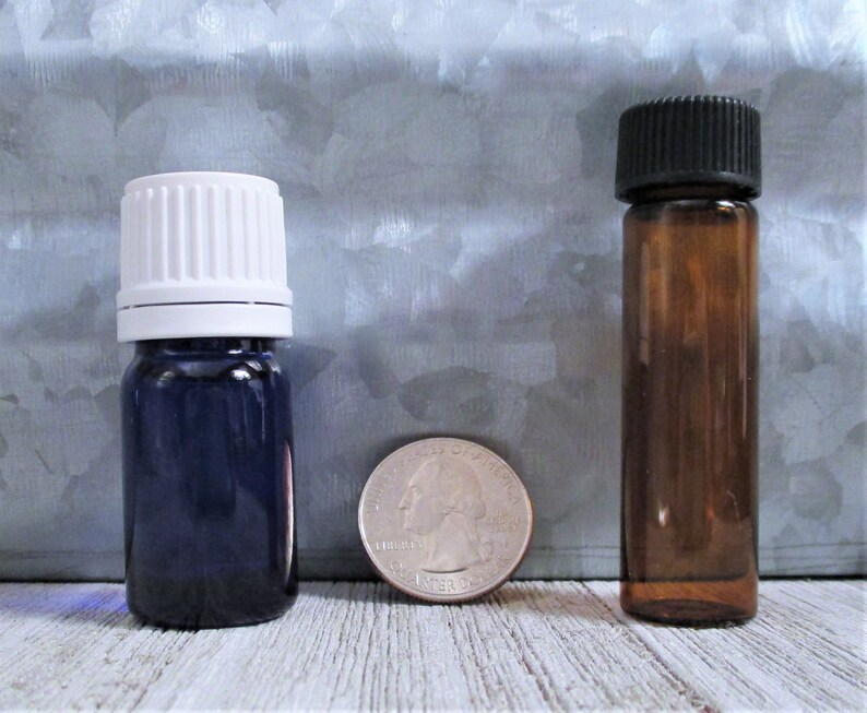 May include: Two glass bottles with different colored caps. The bottle on the left has a white cap and a dark blue body. The bottle on the right has a black cap and a brown body. A US quarter is shown for scale.