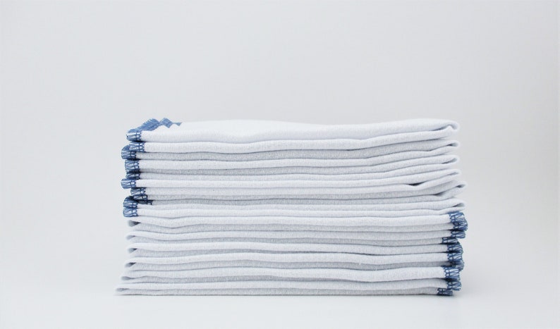 12 white birdseye cotton towels with a border of dusty blue stitching. Each towel is 11.5 inches by 11.5 inches.