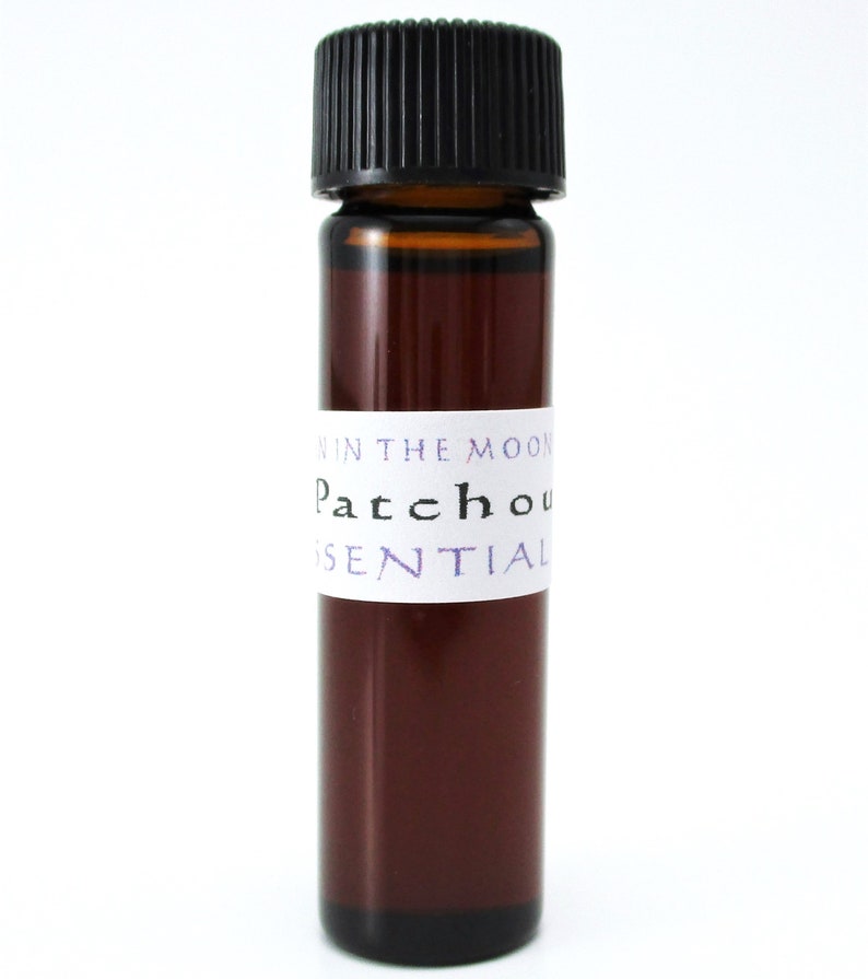 Pode incluir: Um pequeno frasco de vidro castanho com uma tampa preta, etiquetado "Patchouli Essential Oil" em letras brancas com acentos roxos. O r&oacute;tulo tamb&eacute;m diz "In The Moon" em letras menores.