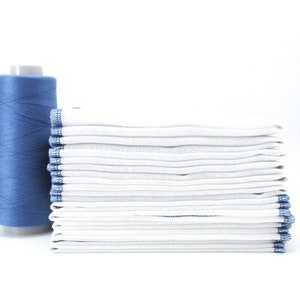 A stack of 12 folded towels with a periwinkle blue border of stitching. The spool of thread in the photo is not included.